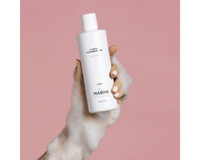 Load image into Gallery viewer, Hand holding a white bottle labeled 'Marini' against a pink background