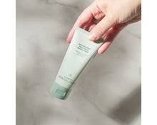 Load image into Gallery viewer, Hand holding a green skincare product bottle on a marble surface
