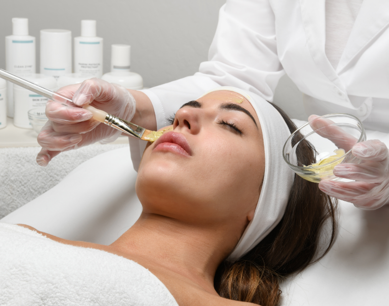 Woman receiving facial treatment with a beautician applying cream to her face.