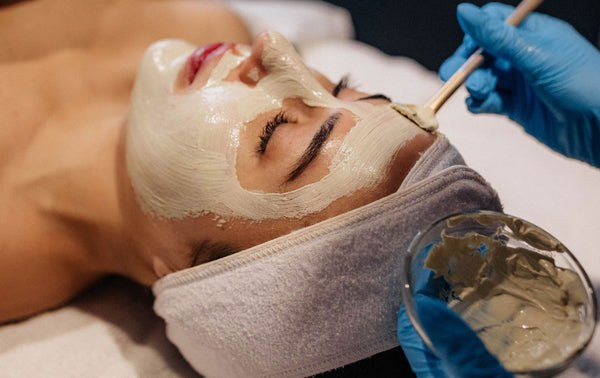 Person receiving a facial mask treatment with a skincare professional applying the mask.