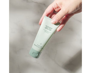 Hand holding a green skincare product bottle on a marble surface
